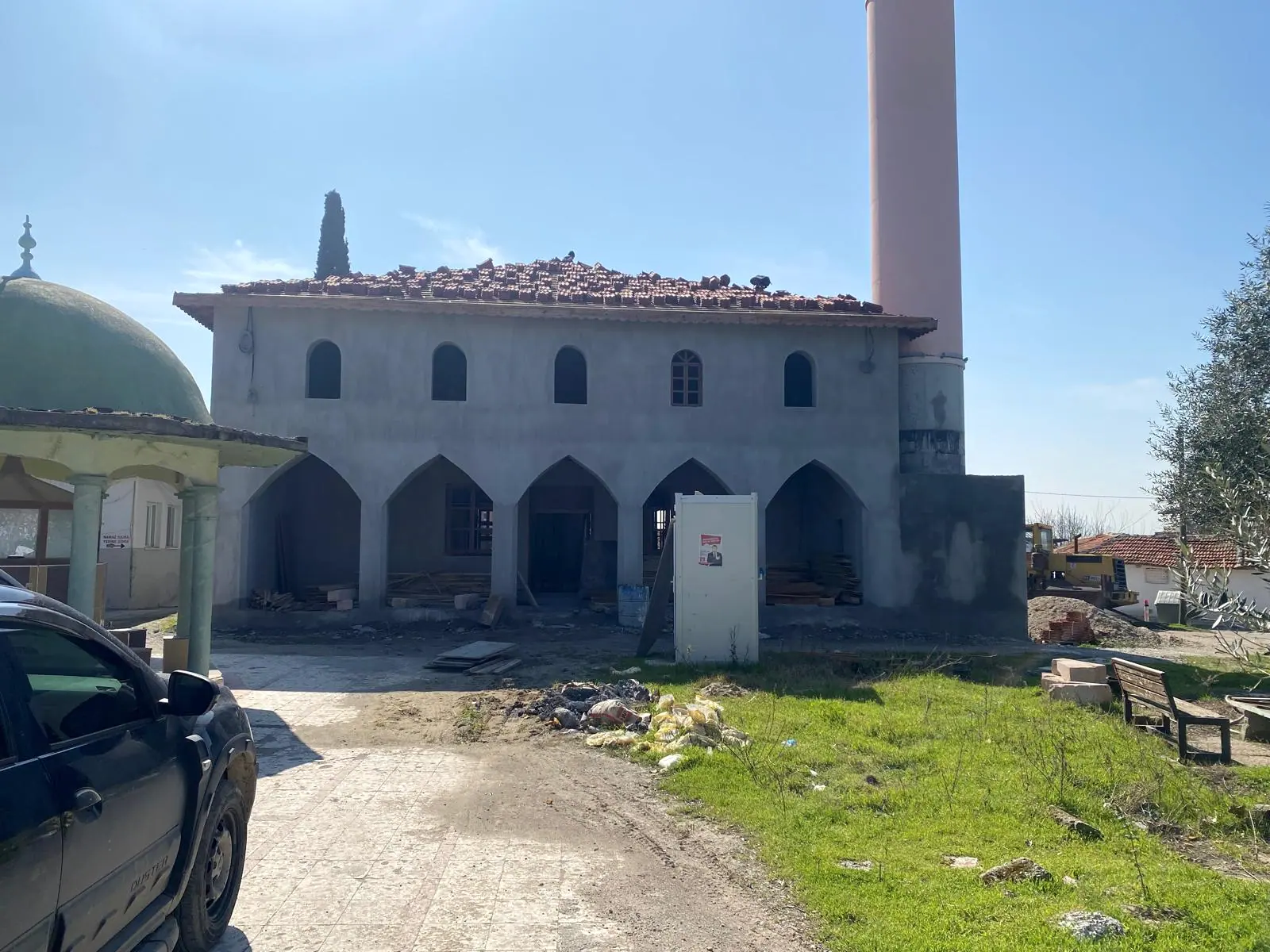 Boyasız sıvalı cami cephesi, yeni serilen kiremit örtü, somon renkli minare gövdesi ve sivri kemerli revak