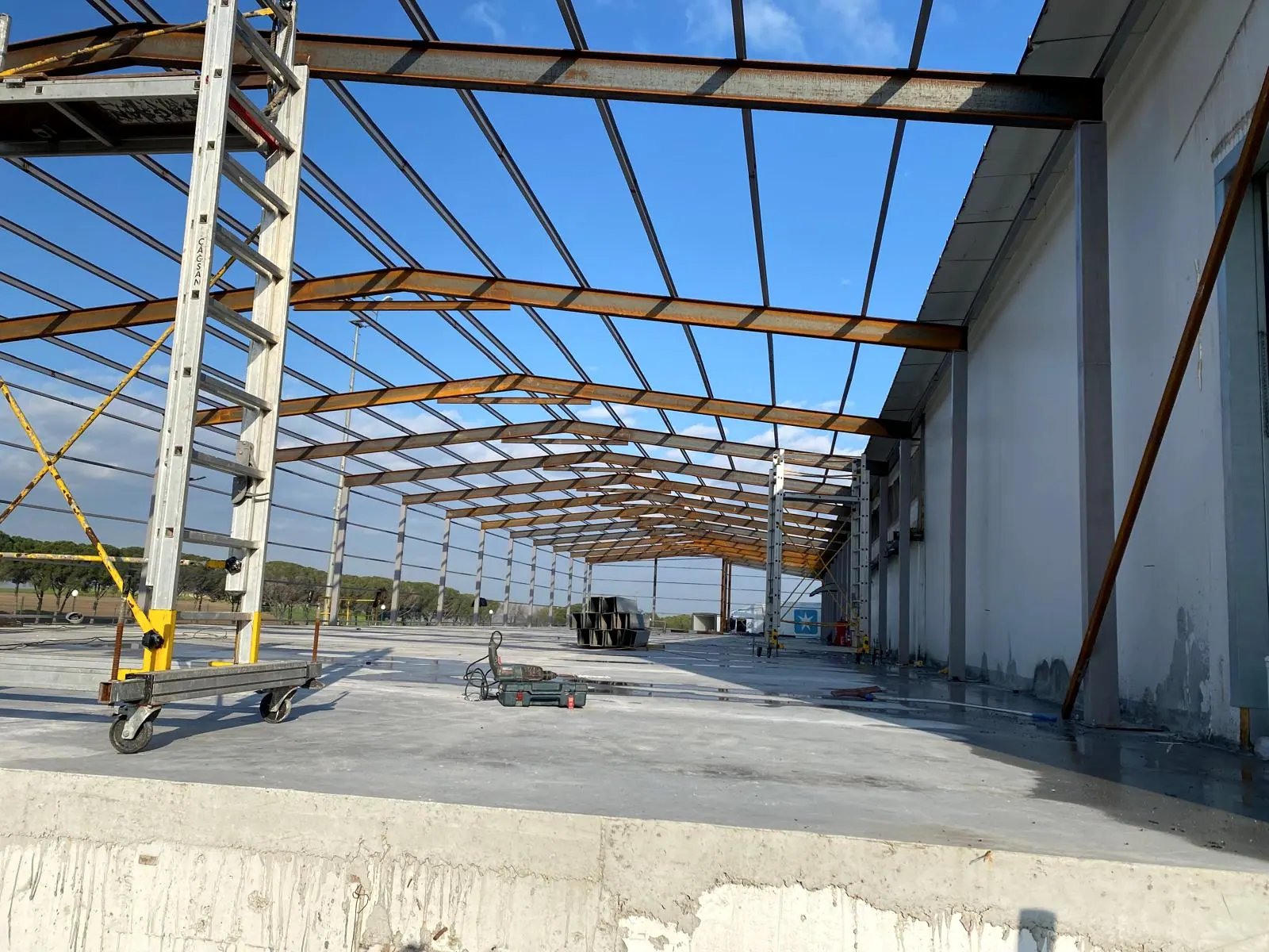 Kaplamasız çelik çatı konstrüksiyonu, aşıklar ve beton zeminde alüminyum merdiven taşıyan seyyar iskele arabası