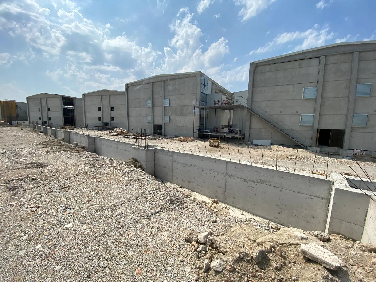 Beton panel duvarlı endüstriyel holler, dış çelik merdiven ve önde filiz donatılı betonarme istinat duvarı