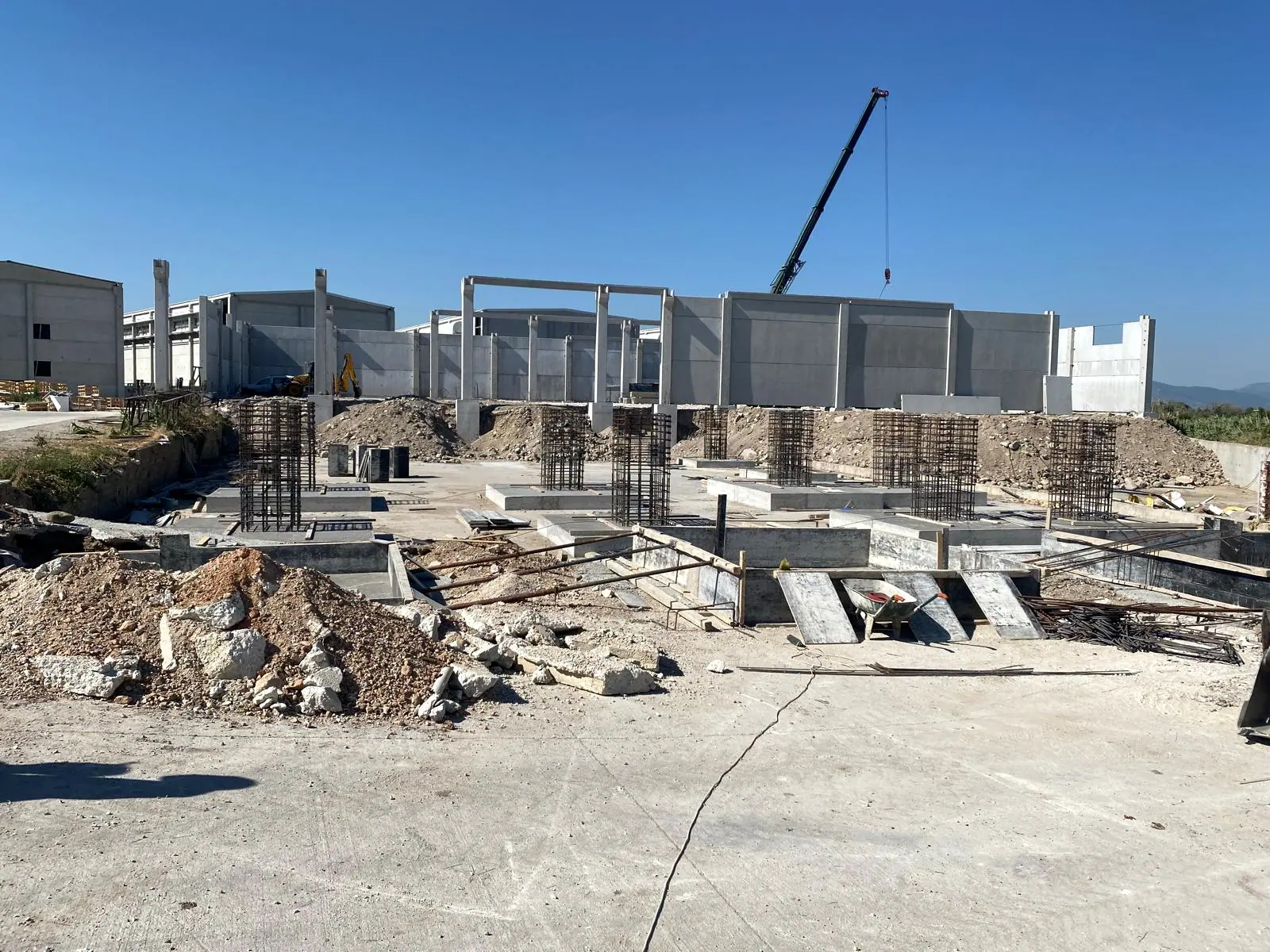 Yeni dökülmüş tekil temeller üzerinde kolon donatı kafesleri, arkada kolonlar arasına yerleştirilmiş beton duvar panelleri