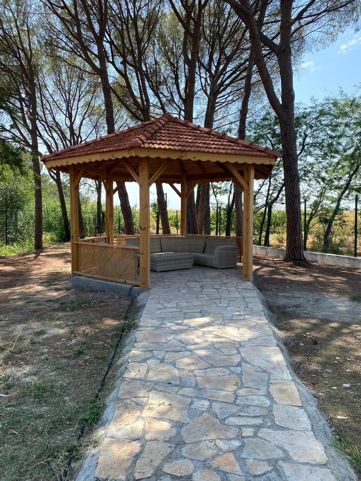 Doğal taş kaplı patikanın ucunda ahşap kamelya, kafes korkuluklar ve gri rattan oturma grubu