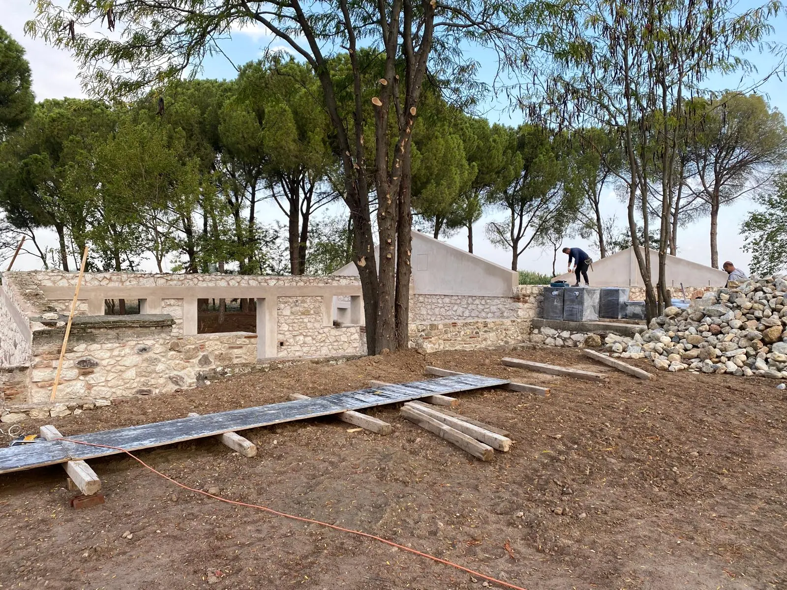 Tuğla hatıllı moloz taş duvarlar, sıvalı lentolu pencere boşlukları ve sağda yığılmış dere taşları