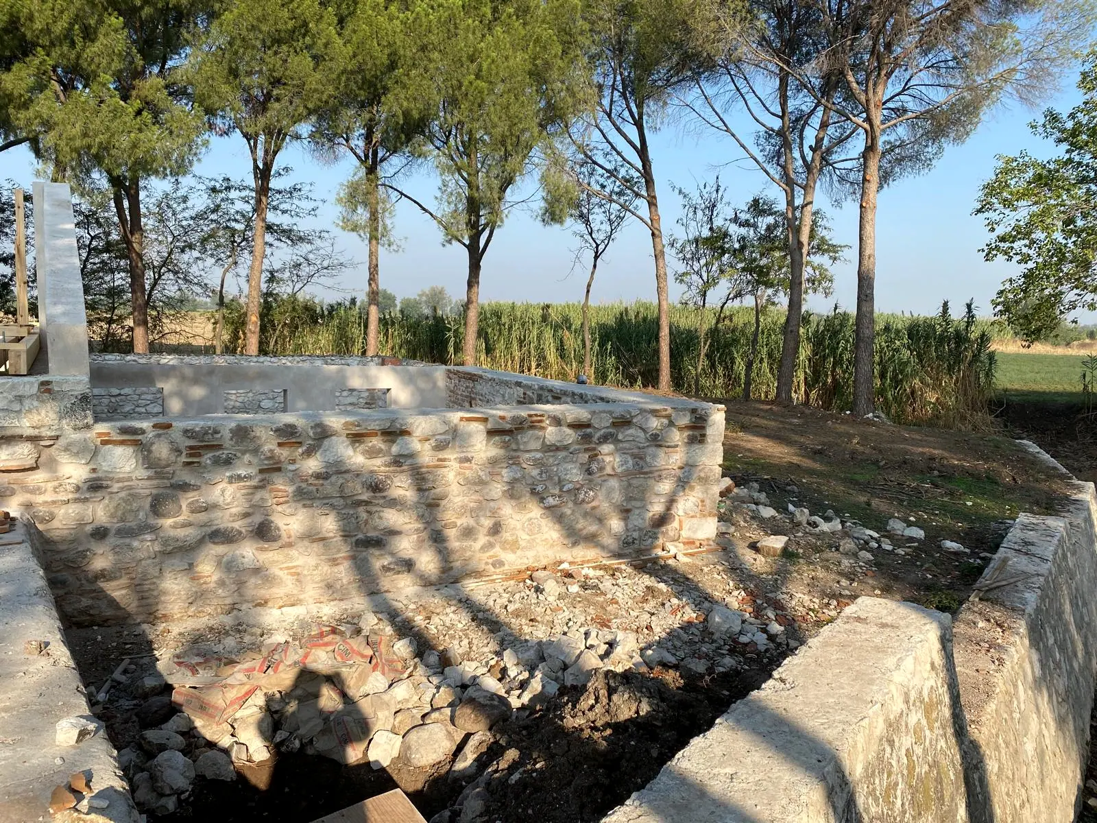 Derzleri yenilenmiş tuğla hatıllı taş duvar, önünde açılmış hendek ve harç torbaları, arkada kamışlık