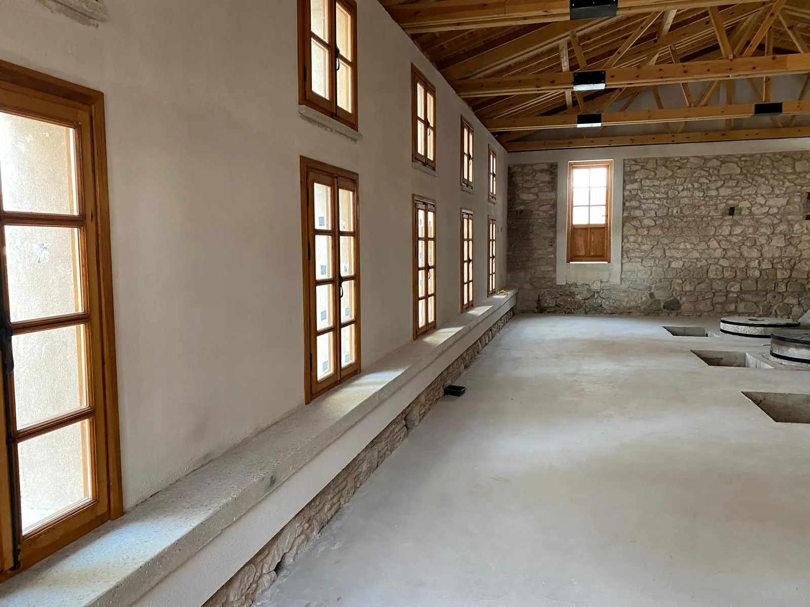 Ahşap makaslı çatı altında uzun salon, iki sıra ahşap pencere, taş duvar ve şap zeminde dikdörtgen açıklıklar