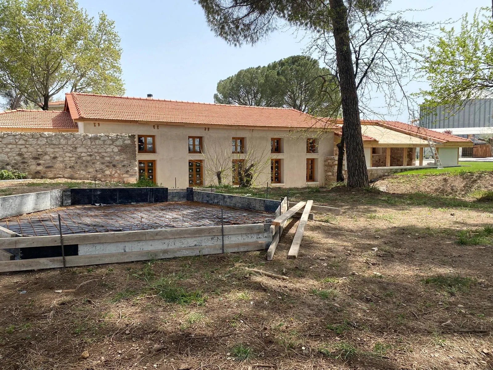Tamamlanmış kiremit çatı ve ahşap doğramalı cephe, önünde donatı serilmiş yeni betonarme döşeme kalıbı