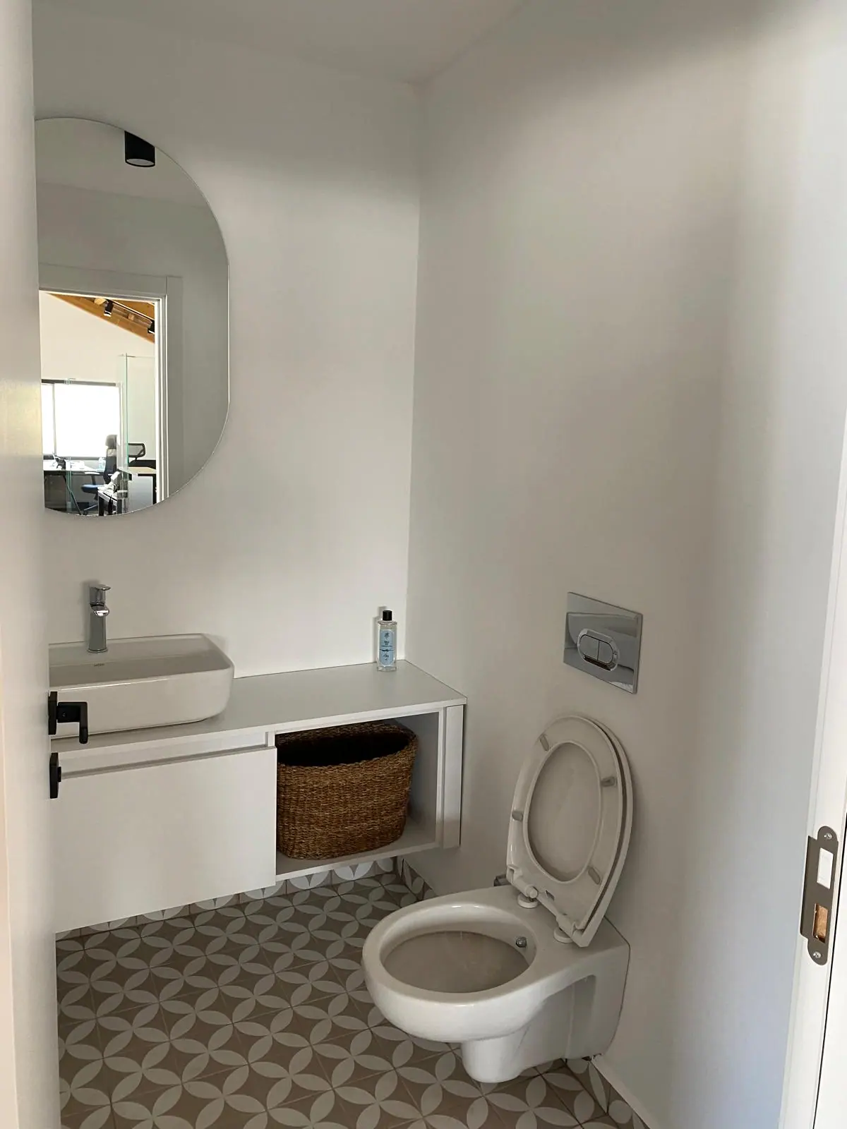 Asma klozet, tezgah üstü lavabo, yuvarlak ayna ve desenli karo zeminli ofis tuvaleti