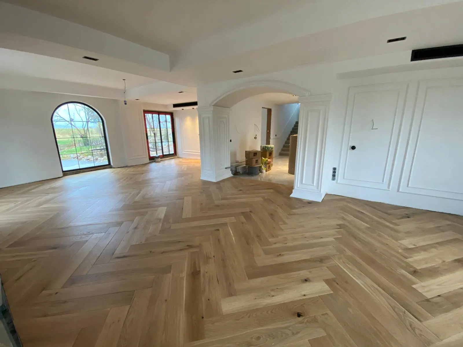 Balıksırtı meşe parke döşenmiş geniş salon, kemerli pencere ve kabartma beyaz duvar panelleri